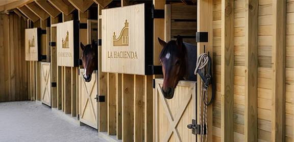 Caballerizas de madera del área ecuestre de La Hacienda Country Club con caballos estabulados.